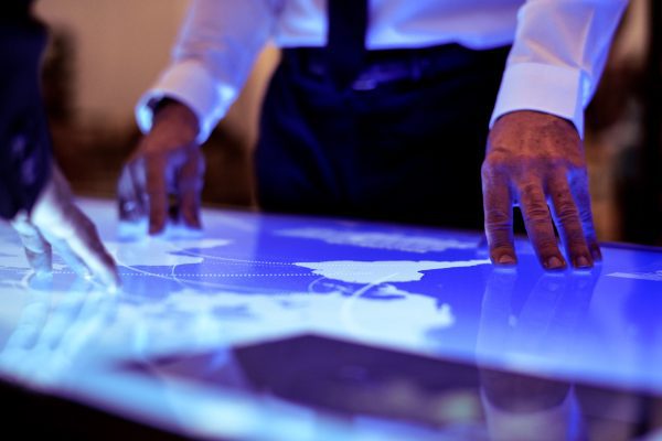 A businessman's hands pointing at a lit up world map projected on a desk