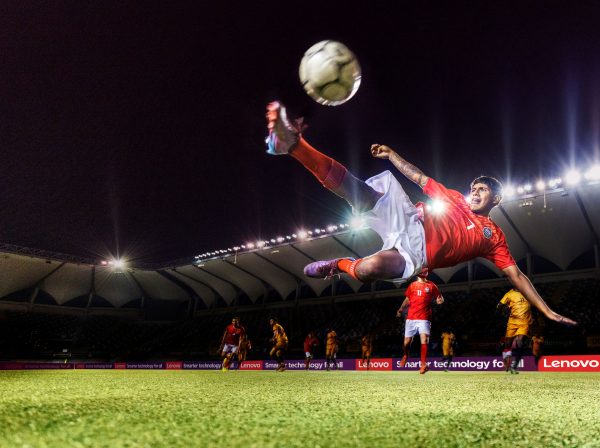 Football player kicking a ball on the pitch -- Lenovo logos in background