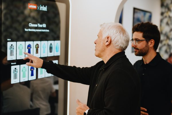 Two men pointing at a digital display with football shirts on.