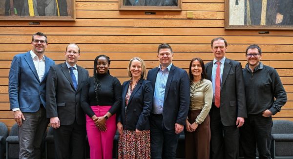 A line of men and women in business smiling at the camera in front of a wooden background
