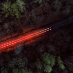 Brand image - A long exposure from a drone shows a light trail of a single car on a road through the forest
